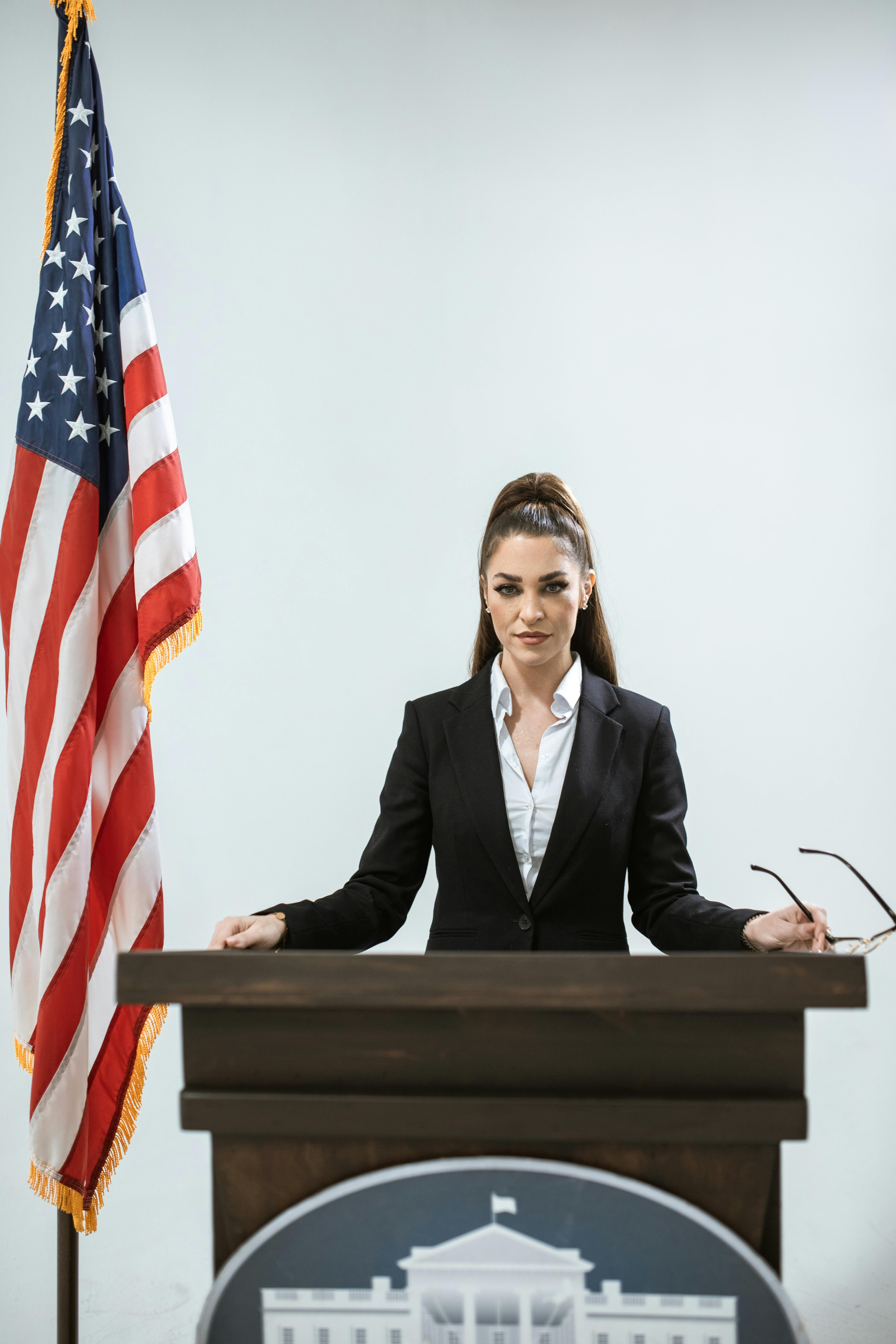 Woman speaking at podium with American flag, symbolizing leadership and diplomacy.